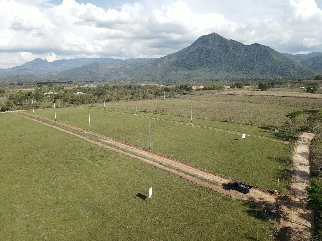 Aerial photograph of the El Volcán land in Ayapa, Yoro: open dirt streets and marker posts across green lots, a mountain behind.