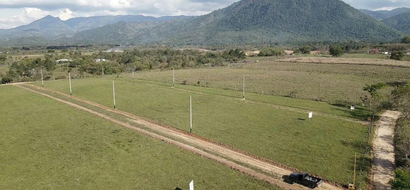 Aerial photograph of the El Volcán land in Ayapa, Yoro: open dirt streets and marker posts across green lots, a mountain behind.