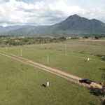 Aerial photograph of the El Volcán land in Ayapa, Yoro: open dirt streets and marker posts across green lots, a mountain behind.
