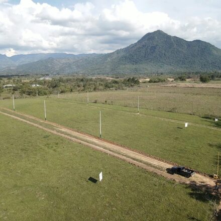 Aerial photograph of the El Volcán land in Ayapa, Yoro: open dirt streets and marker posts across green lots, a mountain behind.