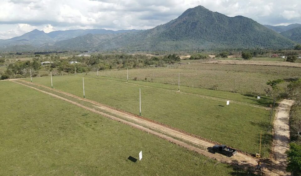 Aerial photograph of the El Volcán land in Ayapa, Yoro: open dirt streets and marker posts across green lots, a mountain behind.