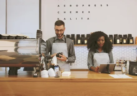 Two café staff behind the counter, one drying a cup, one at a screen