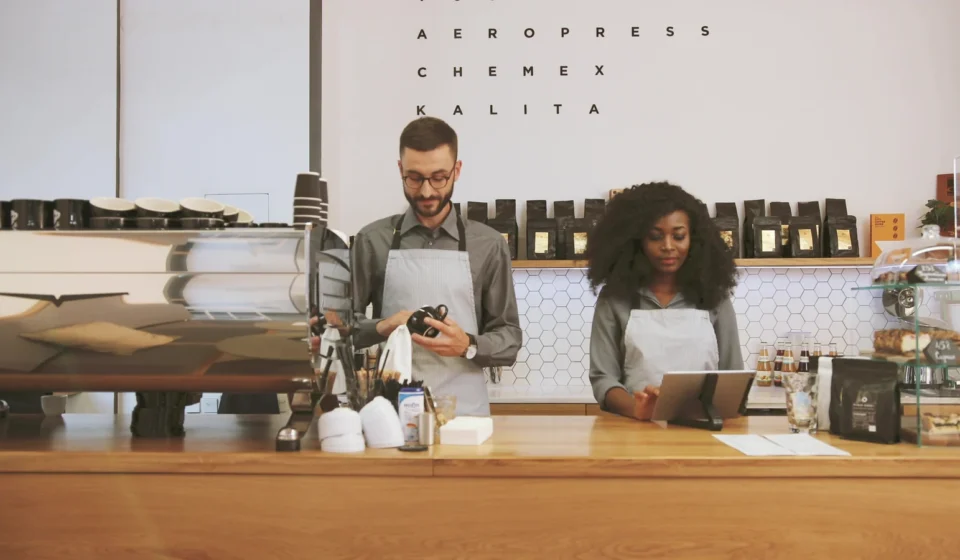 Two café staff behind the counter, one drying a cup, one at a screen
