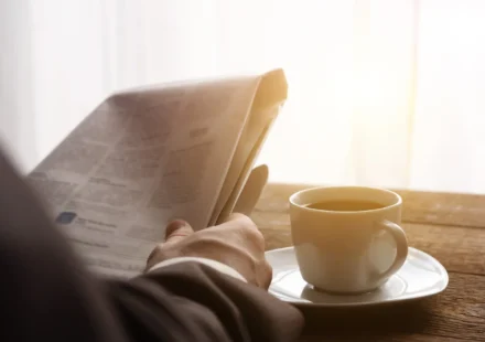 A man reading a newspaper in morning light, a cup of coffee on the table