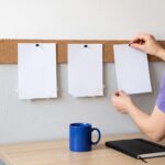 An agency owner pins the third of three blank cards to a cork strip above her desk; the first two were redone.