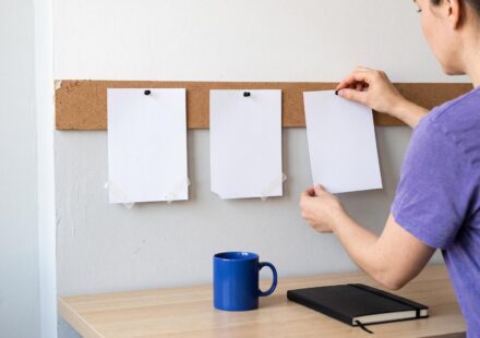 An agency owner pins the third of three blank cards to a cork strip above her desk; the first two were redone.