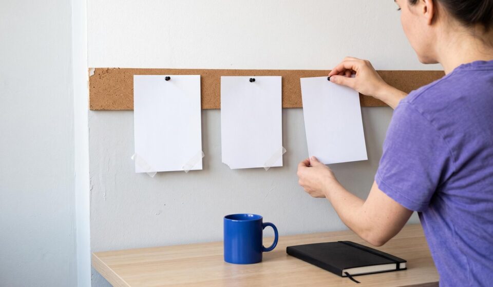 An agency owner pins the third of three blank cards to a cork strip above her desk; the first two were redone.