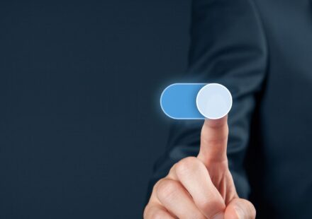 A finger pressing a glowing on-off switch against a dark blue background.